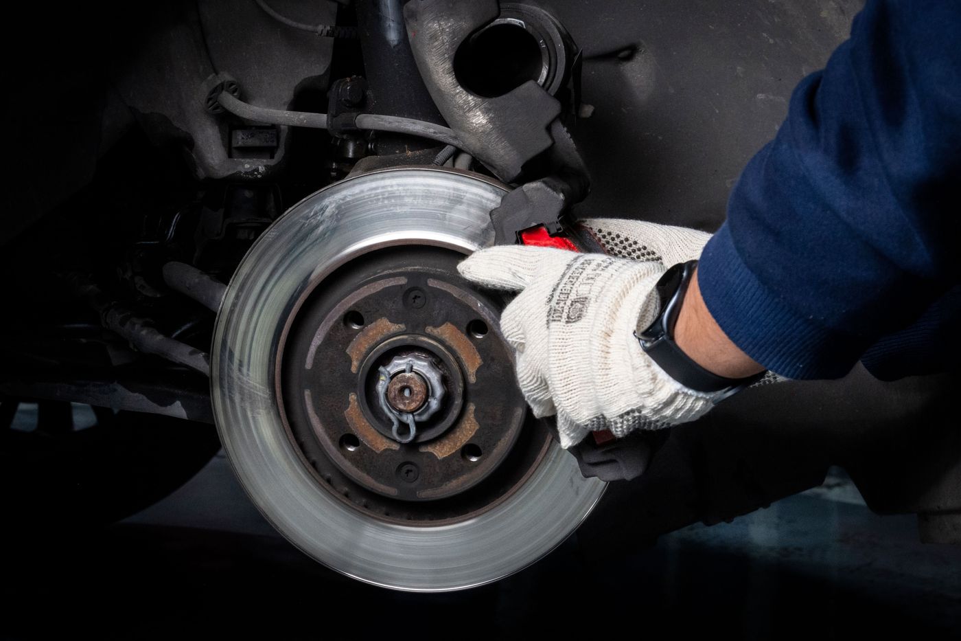 Licensed stock photograph: gloved hands working on a car's brake rotor and caliper with the wheel removed.