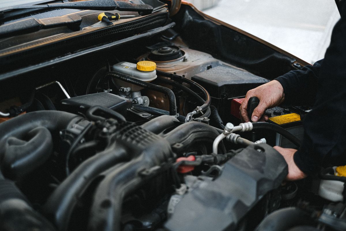 Licensed stock photograph: a hand tightening a battery terminal in an open engine bay.
